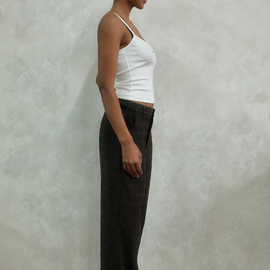 Side profile of model wearing brown windowpane plaid Carter Pants with white LÉLA tank top and gold hoop earrings against textured white wall