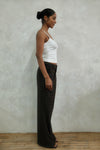 Side profile of model wearing brown windowpane plaid Carter Pants with white LÉLA tank top and gold hoop earrings against textured white wall