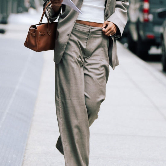 Model wearing beige Carter Pants with matching blazer, white LÉLA tank top and brown leather handbag on city street