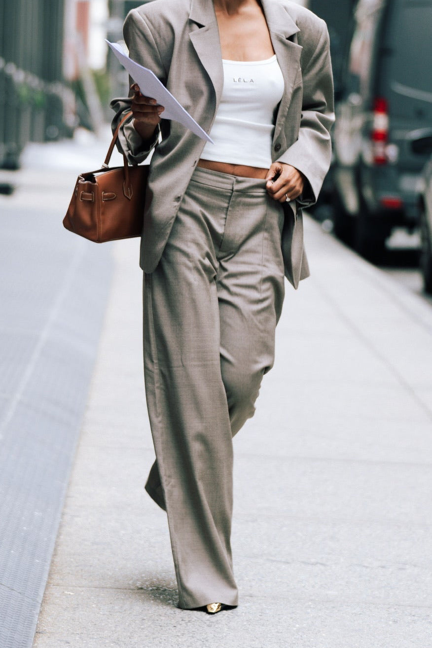 Model wearing beige Carter Pants with matching blazer, white LÉLA tank top and brown leather handbag on city street