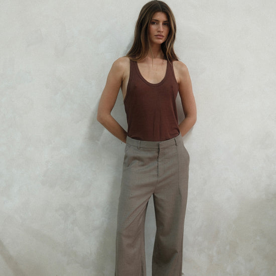 Full-length view of model wearing beige Carter Pants with brown ribbed tank top against white background, showing wide-leg silhouette and tailored fit