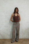 Full-length view of model wearing beige Carter Pants with brown ribbed tank top against white background, showing wide-leg silhouette and tailored fit
