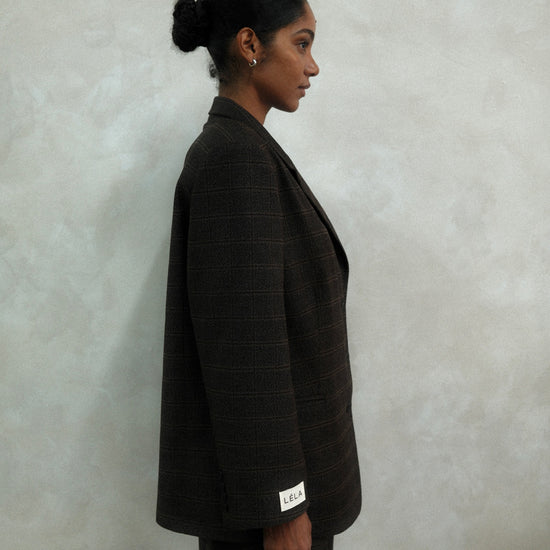 Side view of model wearing brown windowpane plaid Archer Blazer with white LÉLA branded label visible on cuff, styled with matching pants