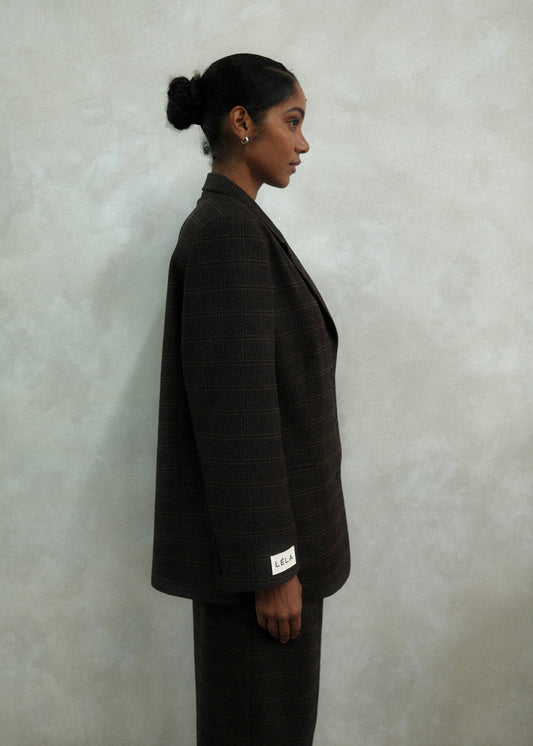 Side view of model wearing brown windowpane plaid Archer Blazer with white LÉLA branded label visible on cuff, styled with matching pants