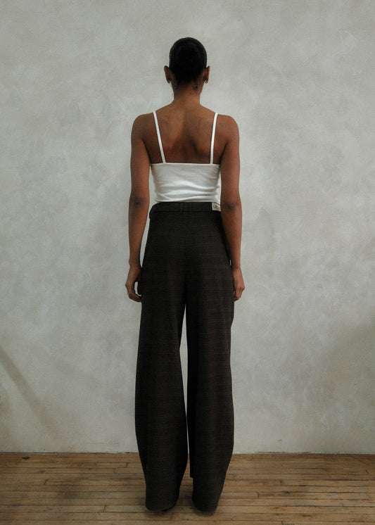 Back view of model wearing brown windowpane plaid Carter Pants with white ribbed tank top, showing wide-leg silhouette against textured white wall