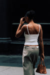 Back view of a woman walking away wearing the white ribbed LÉLA tank top and beige LÉLA Archer trousers with a LÉLA label on the rear waistband, holding a brown leather handbag