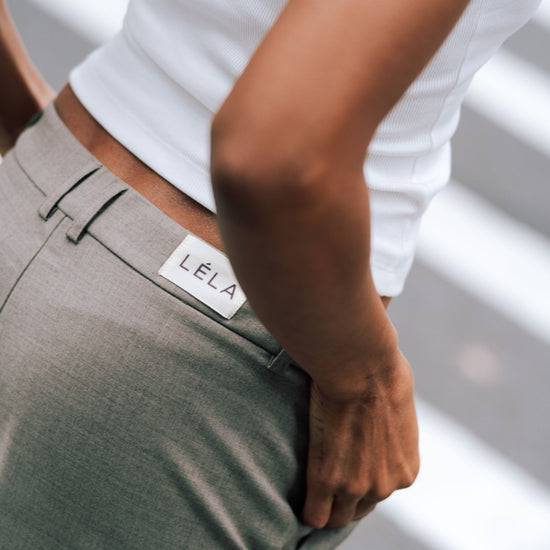 Close-up detail of beige Carter Pants showing LÉLA branded label at waistband, styled with white LÉLA tank top