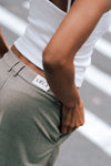 Close-up detail of beige Carter Pants showing LÉLA branded label at waistband, styled with white LÉLA tank top