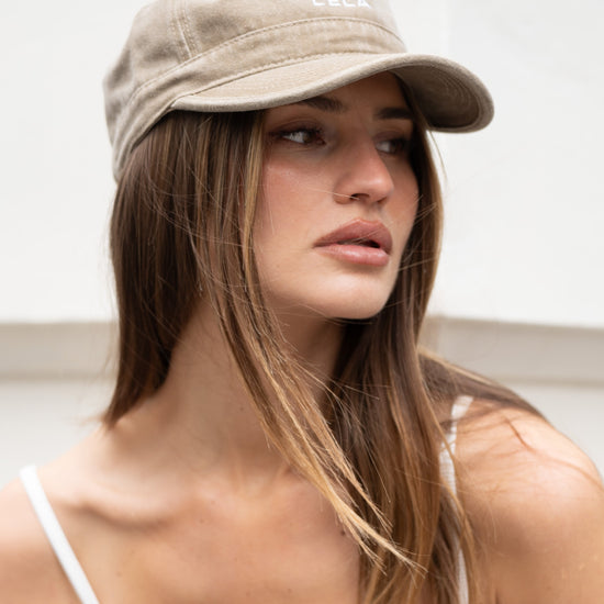 Close-up front view of washed army green LÉLA cap with embroidered white logo, worn with white tank top against minimal white background