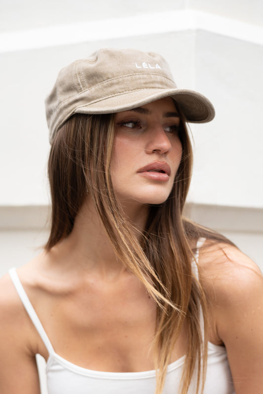 Close-up front view of washed army green LÉLA cap with embroidered white logo, worn with white tank top against minimal white background