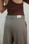 Back detail view of beige Carter Pants showing LÉLA branded label on waistband, styled with brown tank top against white background