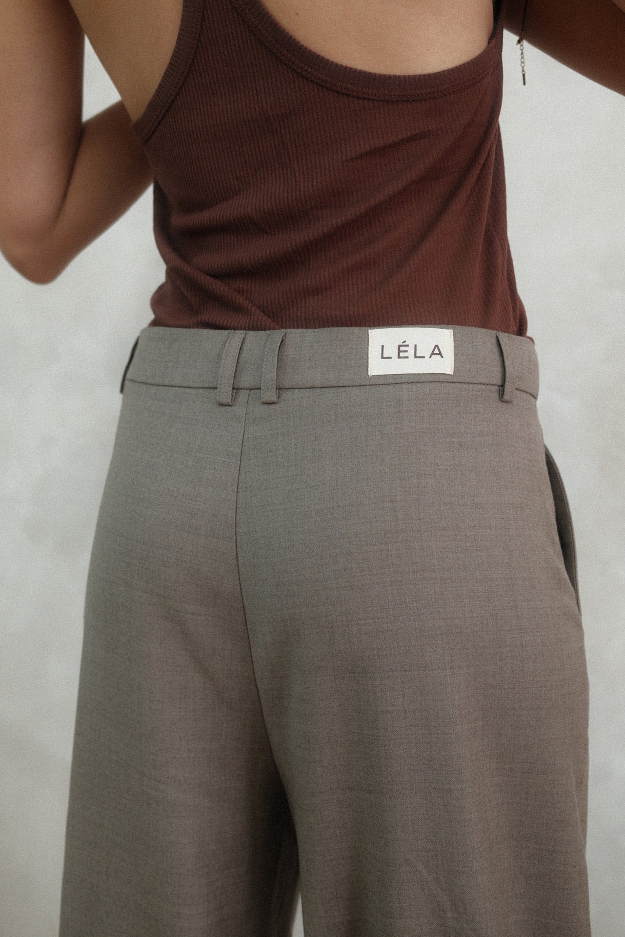 Back detail view of beige Carter Pants showing LÉLA branded label on waistband, styled with brown tank top against white background