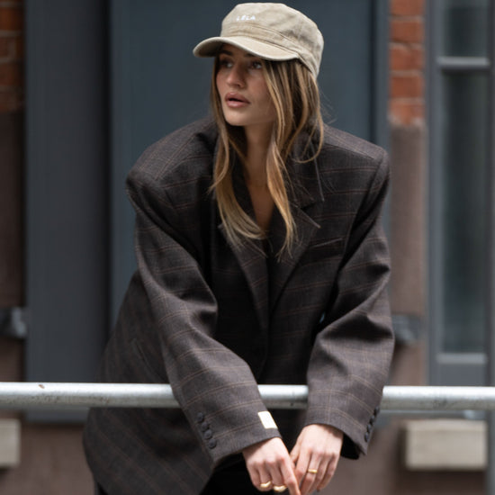 Model wearing washed army green LÉLA cap styled with oversized brown LÉLA Archer blazer in urban setting