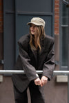 Model wearing washed army green LÉLA cap styled with oversized brown LÉLA Archer blazer in urban setting