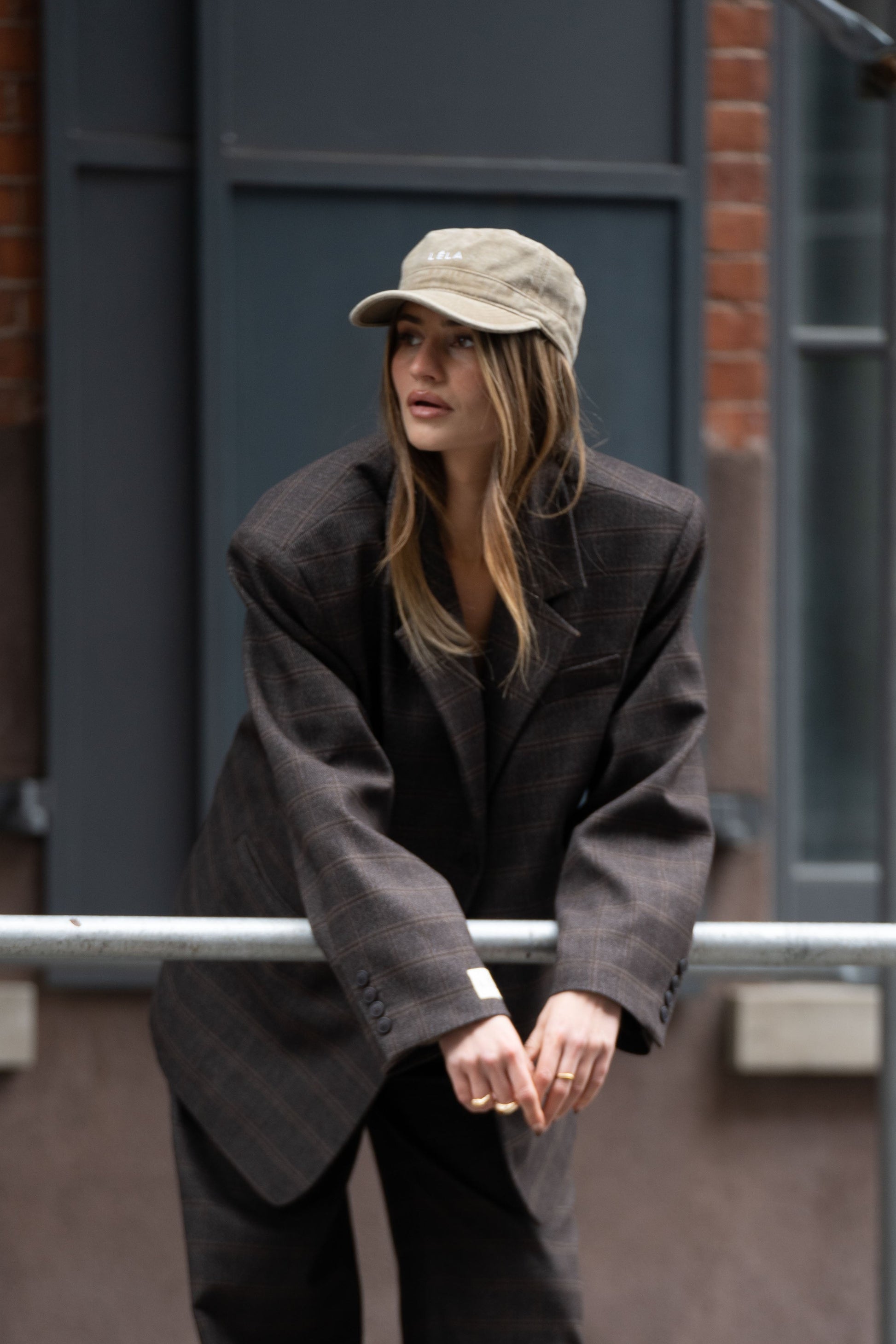 Model wearing washed army green LÉLA cap styled with oversized brown LÉLA Archer blazer in urban setting