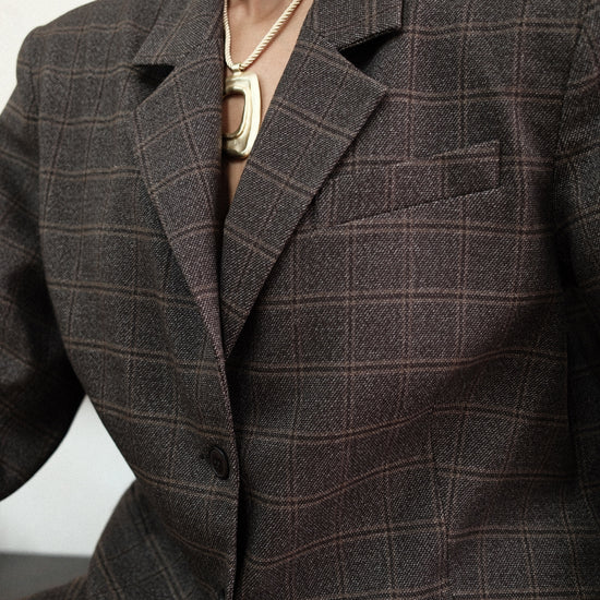 Close-up detail of brown windowpane plaid Archer Blazer showing notched lapel and textured fabric, styled with gold chain necklace