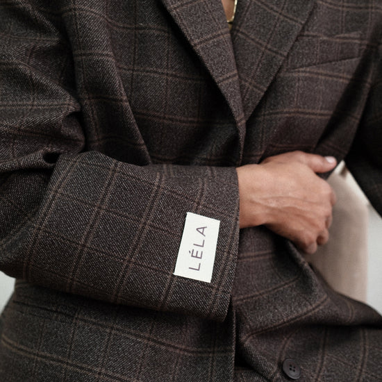 Close-up detail of brown windowpane plaid Archer Blazer showing white LÉLA branded label patch on cuff