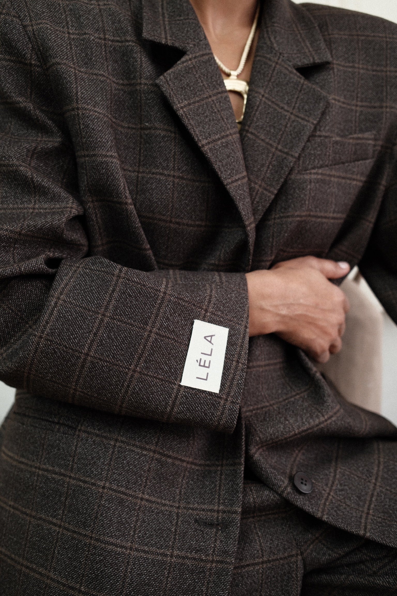 Close-up detail of brown windowpane plaid Archer Blazer showing white LÉLA branded label patch on cuff