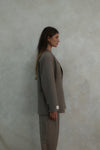 Side profile of model wearing beige Carter Blazer with matching pants and LÉLA label visible on cuff against textured white background