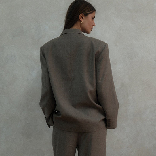 Back view of beige Carter Blazer showing tailored silhouette and length, styled with matching pants against textured white background