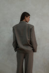 Back view of beige Carter Blazer showing tailored silhouette and length, styled with matching pants against textured white background