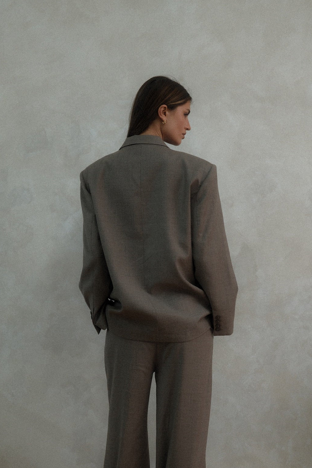 Back view of beige Carter Blazer showing tailored silhouette and length, styled with matching pants against textured white background