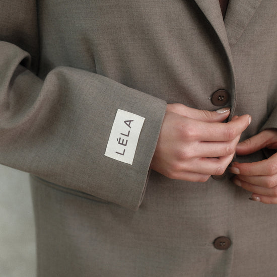 Close-up of beige Carter Blazer sleeve showing white LÉLA branded label patch with three-button closure detail