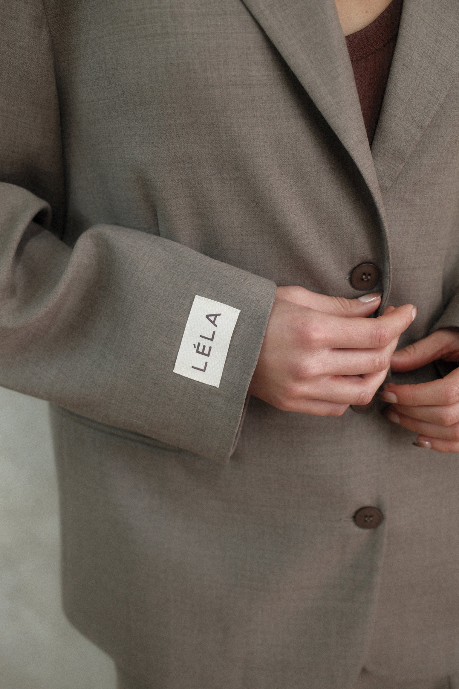 Close-up of beige Carter Blazer sleeve showing white LÉLA branded label patch with three-button closure detail