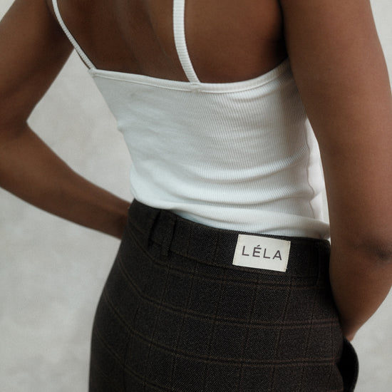 Back detail view of black textured Carter Pants showing LÉLA branded label on waistband, styled with white LÉLA tank top against white background