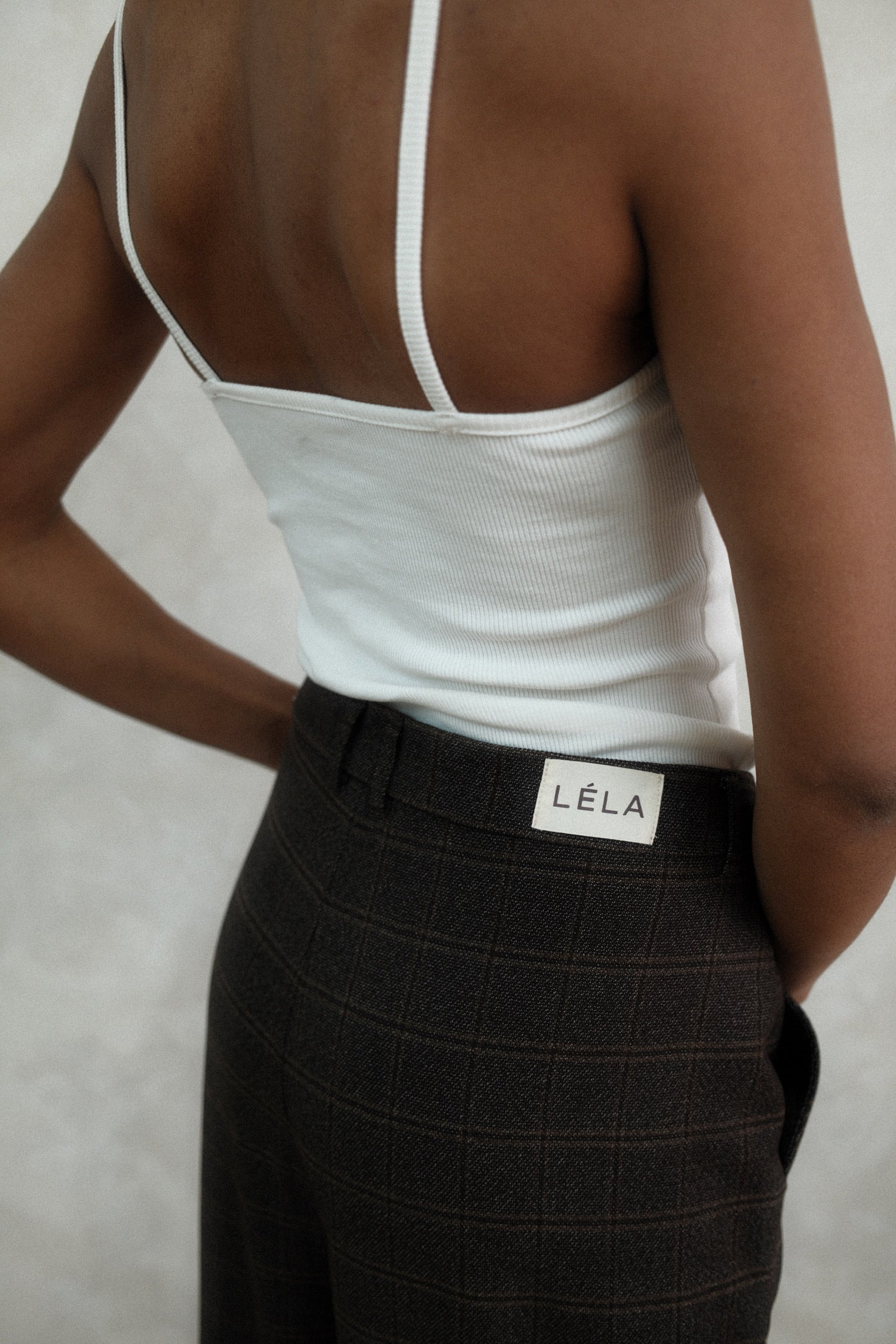 Back detail view of black textured Carter Pants showing LÉLA branded label on waistband, styled with white LÉLA tank top against white background