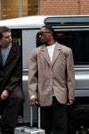 Male Model wearing beige Carter Blazer with black sunglasses, white t-shirt and silver luggage, standing by silver van with another person on his right