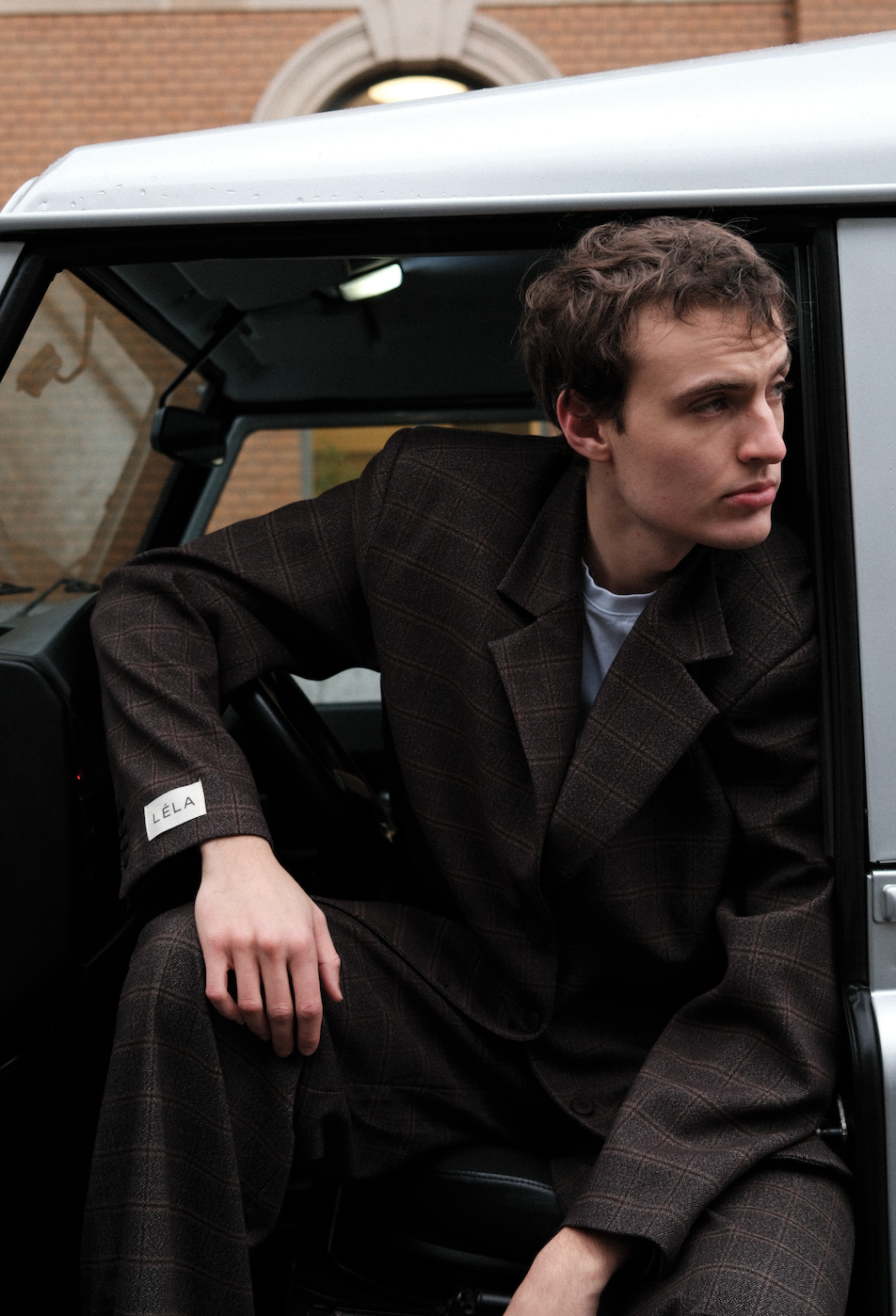 Male Model wearing brown windowpane plaid Archer Blazer styled with matching pants, sitting in silver car