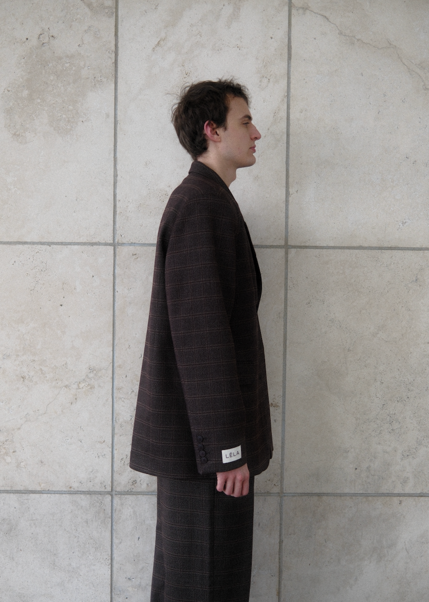 Side view of male model wearing brown windowpane plaid Archer Blazer with white LÉLA branded label visible on cuff, styled with matching pants