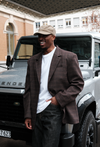 Male Model wearing brown windowpane plaid Archer Blazer styled with white t-shirt, dark denim pants, and washed army green LÉLA cap, in front of silver Land Rover Defender