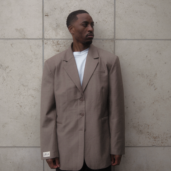 Three-quarter view of model wearing beige Carter Blazer with white t-shirt and dark denim, showing relaxed oversized silhouette against concrete wall