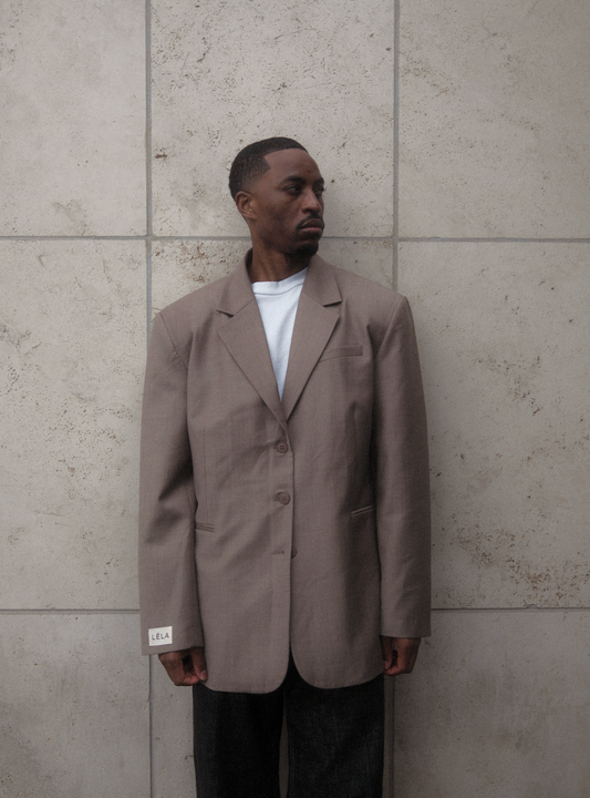 Three-quarter view of model wearing beige Carter Blazer with white t-shirt and dark denim, showing relaxed oversized silhouette against concrete wall