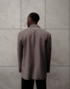 Back view of beige Carter Blazer showing tailored construction and length, styled with dark denim against textured concrete wall